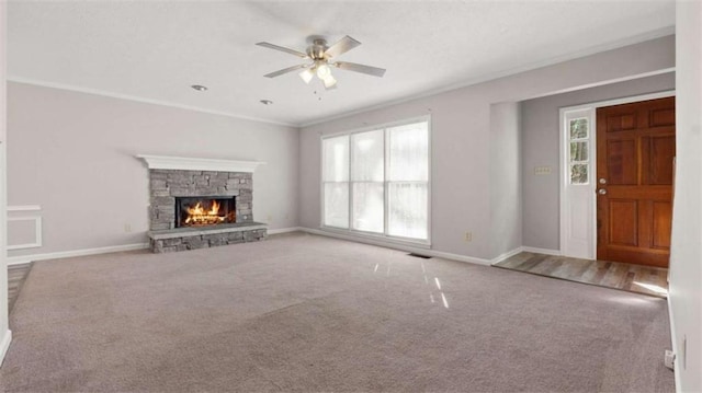 unfurnished living room featuring carpet floors, baseboards, crown molding, and a stone fireplace