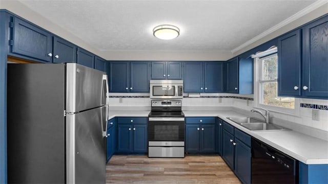 kitchen with appliances with stainless steel finishes, a sink, light wood-style floors, and blue cabinets