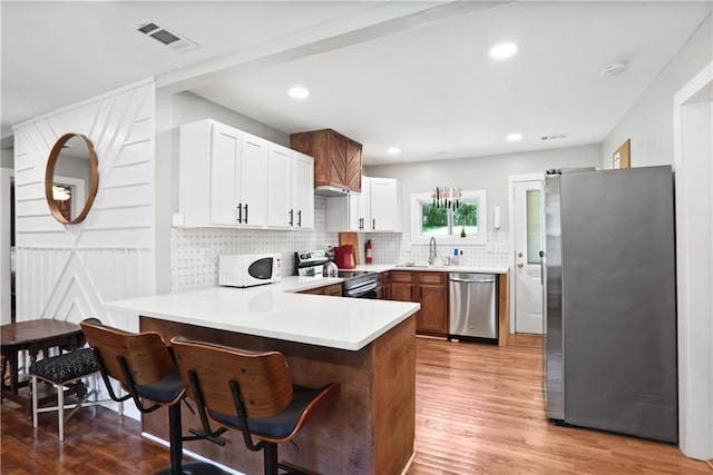 1202 Key Rd SE, Atlanta, GA 30316 - kitchen featuring appliances with stainless steel finishes, a peninsula, a sink, light wood-type flooring, and tasteful backsplash