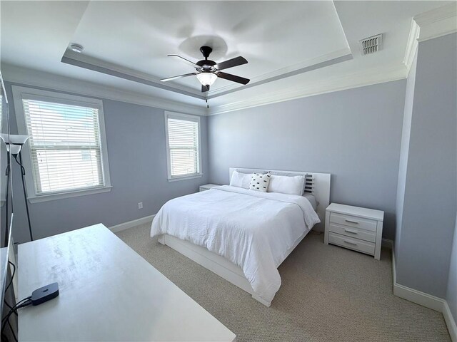 carpeted bedroom featuring a tray ceiling, crown molding, baseboards, and a ceiling fan