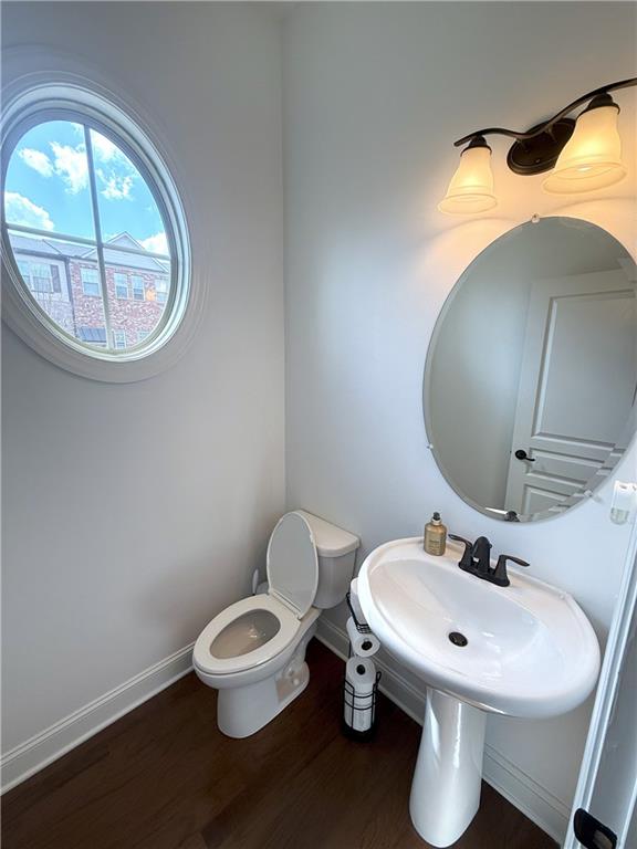 half bathroom featuring toilet, wood finished floors, and baseboards