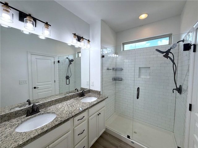 full bath with a stall shower, double vanity, a sink, and wood finished floors