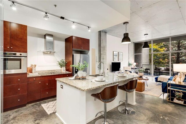 kitchen featuring decorative light fixtures, sink, light stone countertops, stainless steel appliances, and wall chimney exhaust hood