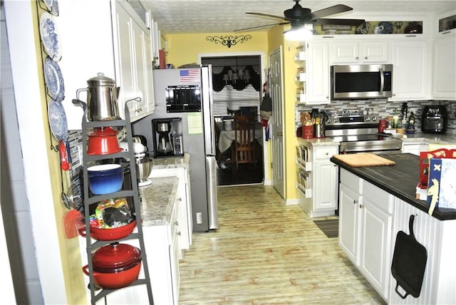 kitchen with appliances with stainless steel finishes, decorative backsplash, white cabinets, light wood-type flooring, and ceiling fan