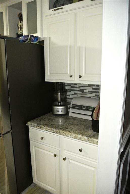 kitchen with decorative backsplash, white cabinets, light stone counters, and stainless steel refrigerator