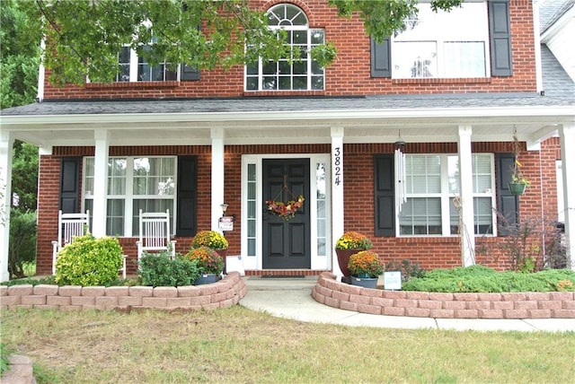 doorway to property with a porch and a yard