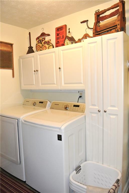 laundry room featuring a textured ceiling, dark wood-type flooring, washing machine and clothes dryer, and cabinets