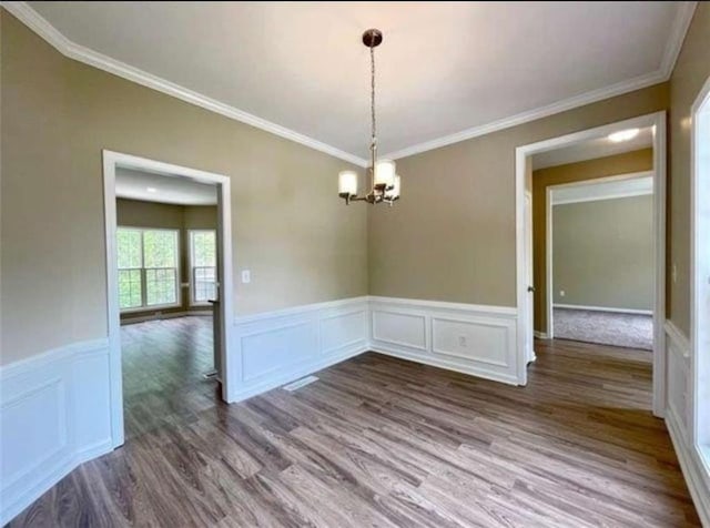 unfurnished dining area featuring an inviting chandelier, crown molding, and hardwood / wood-style floors