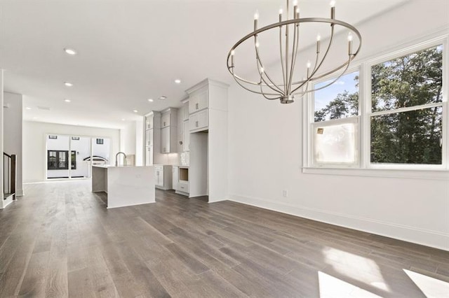 unfurnished living room with an inviting chandelier, sink, and dark hardwood / wood-style flooring