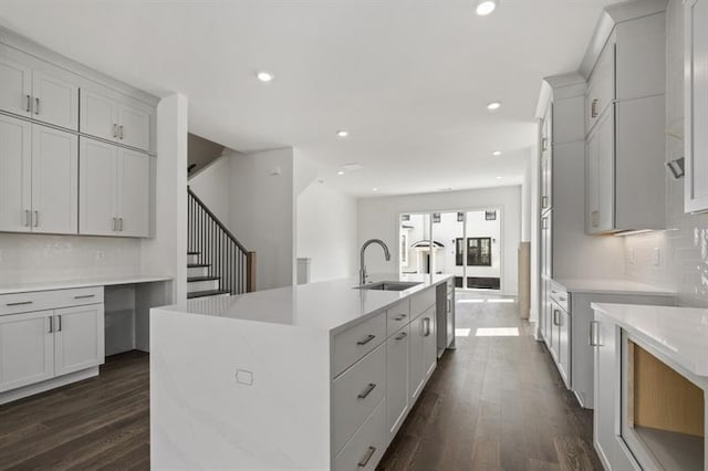 kitchen with sink, dark hardwood / wood-style floors, tasteful backsplash, and an island with sink