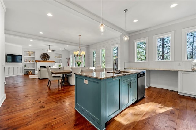 kitchen with pendant lighting, beamed ceiling, an island with sink, sink, and light stone countertops