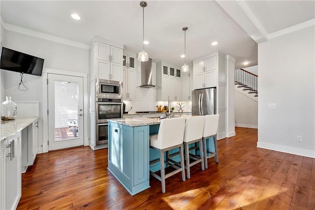 kitchen featuring wall chimney exhaust hood, stainless steel appliances, light stone countertops, and a center island with sink