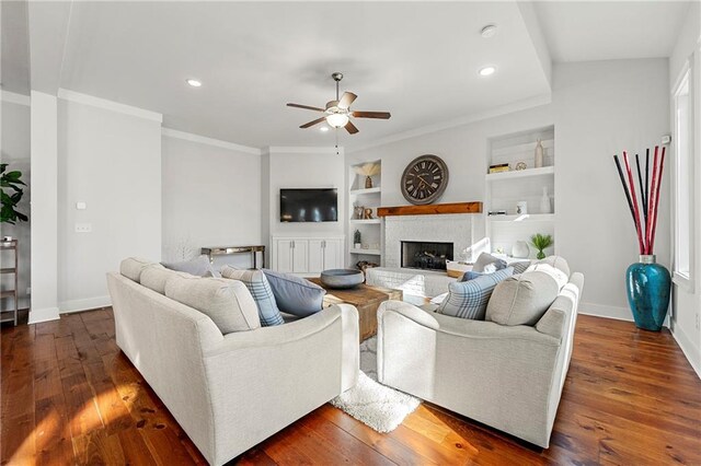 living room featuring dark hardwood / wood-style flooring, built in shelves, ornamental molding, and ceiling fan