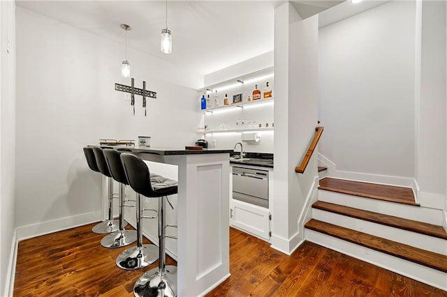 bar with dark wood-type flooring, white cabinetry, sink, and hanging light fixtures