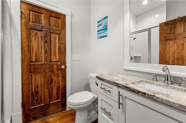 bathroom with hardwood / wood-style flooring, vanity, toilet, and a shower with shower door