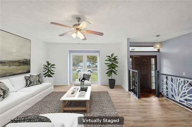 living room featuring ceiling fan, a textured ceiling, and light wood-type flooring