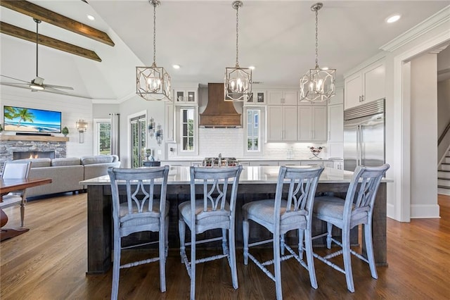 kitchen featuring dark wood-style floors, vaulted ceiling with beams, a fireplace, decorative backsplash, and premium range hood