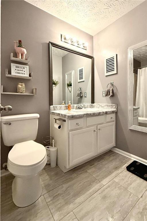 full bath with vanity, baseboards, a textured ceiling, toilet, and visible vents