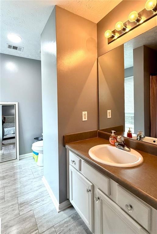 bathroom featuring a textured ceiling, vanity, baseboards, and visible vents