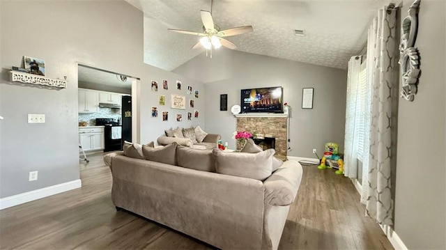 living room featuring ceiling fan, light wood-style flooring, a textured ceiling, a stone fireplace, and vaulted ceiling