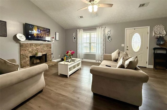 living room with a fireplace, visible vents, ceiling fan, lofted ceiling, and wood finished floors