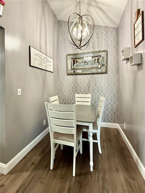 dining room with baseboards, an inviting chandelier, a textured ceiling, an accent wall, and wood finished floors