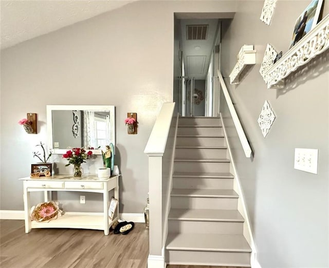 staircase featuring wood finished floors, baseboards, and visible vents