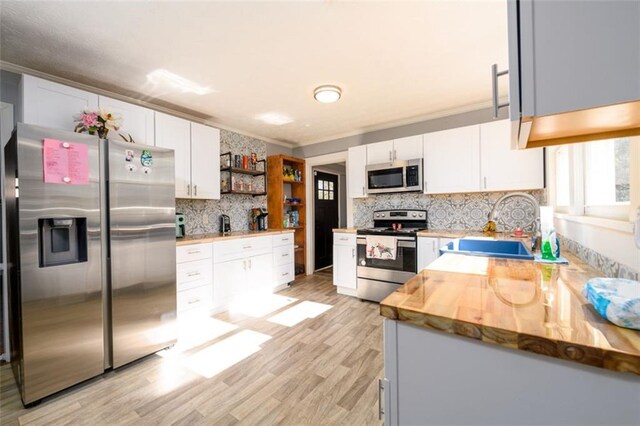 kitchen featuring decorative backsplash, stainless steel appliances, wooden counters, white cabinetry, and light hardwood / wood-style flooring