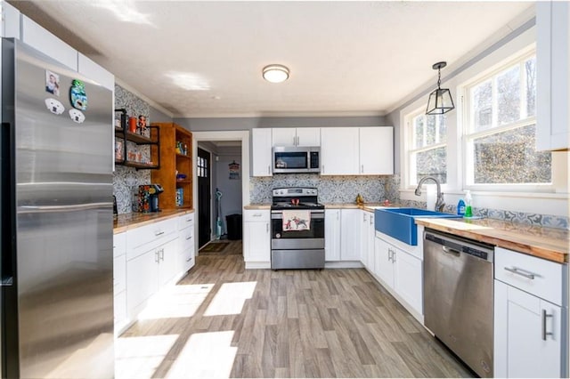 kitchen with stainless steel appliances, light hardwood / wood-style floors, decorative light fixtures, and white cabinetry