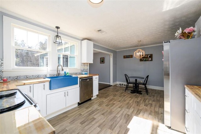 kitchen with pendant lighting, sink, white cabinetry, appliances with stainless steel finishes, and butcher block counters