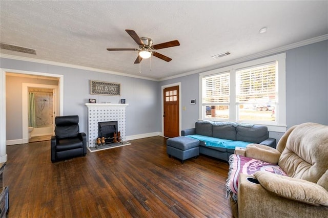 living room with ceiling fan, dark wood-type flooring, crown molding, a tile fireplace, and a textured ceiling