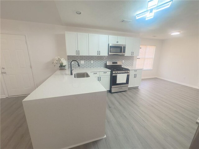 kitchen with sink, white cabinetry, vaulted ceiling, appliances with stainless steel finishes, and kitchen peninsula