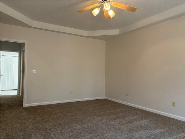 empty room featuring baseboards, dark colored carpet, a ceiling fan, and a raised ceiling