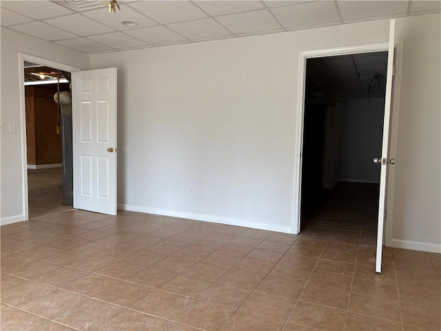 unfurnished bedroom featuring a walk in closet, tile patterned flooring, a drop ceiling, and baseboards