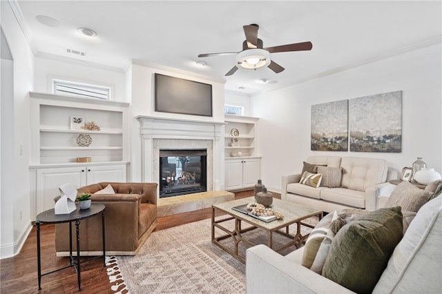 living area featuring visible vents, built in shelves, wood finished floors, crown molding, and a premium fireplace