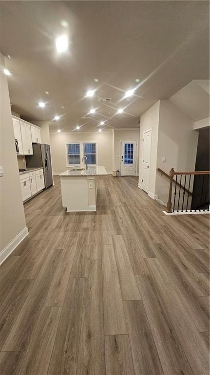 kitchen featuring light wood-type flooring, a kitchen island with sink, stainless steel fridge with ice dispenser, and white cabinetry