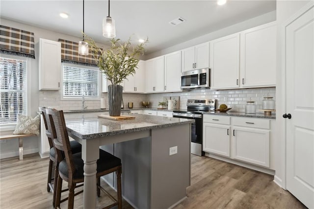 kitchen featuring a center island, stainless steel appliances, white cabinetry, and dark stone counters