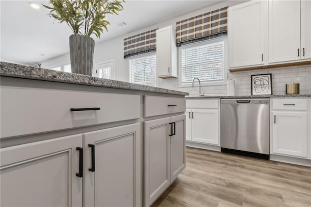 kitchen with decorative backsplash, light stone countertops, light hardwood / wood-style flooring, dishwasher, and white cabinetry