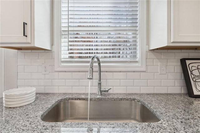 interior details featuring white cabinetry, sink, and light stone counters