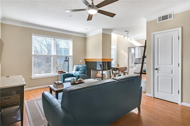 living room featuring ornamental molding, a textured ceiling, ceiling fan, light hardwood / wood-style flooring, and a fireplace