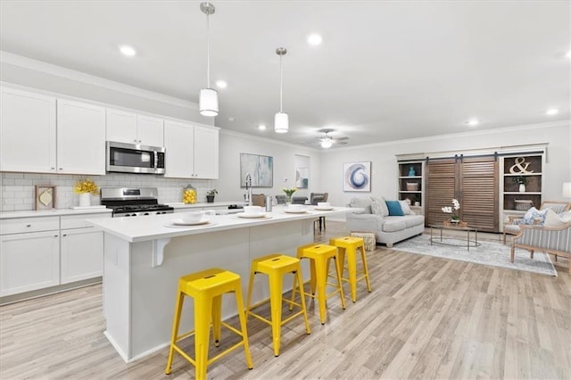 kitchen featuring white cabinetry, appliances with stainless steel finishes, open floor plan, and ornamental molding