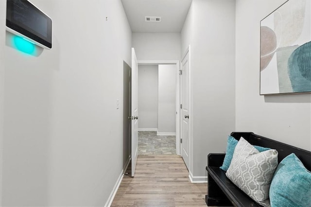 corridor featuring baseboards, visible vents, and light wood finished floors