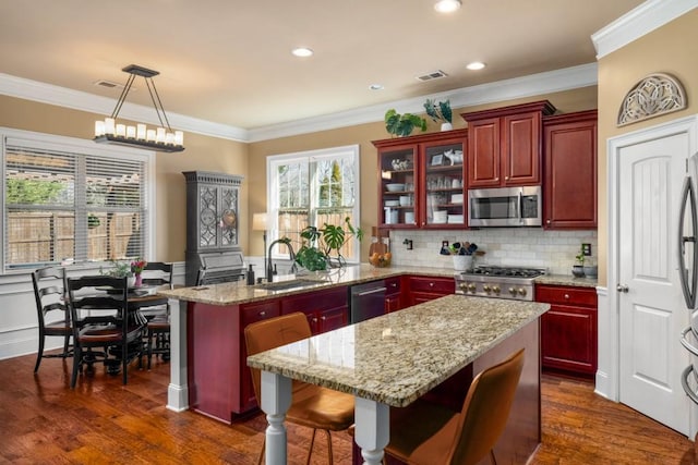 kitchen with reddish brown cabinets, a peninsula, appliances with stainless steel finishes, and a sink