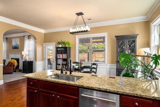 kitchen with arched walkways, wainscoting, dark brown cabinets, a fireplace, and a sink