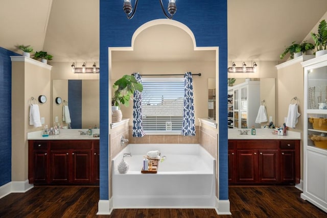 bathroom featuring two vanities, a garden tub, a sink, and wood finished floors