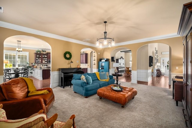 living room featuring arched walkways, ornamental molding, a notable chandelier, and wainscoting