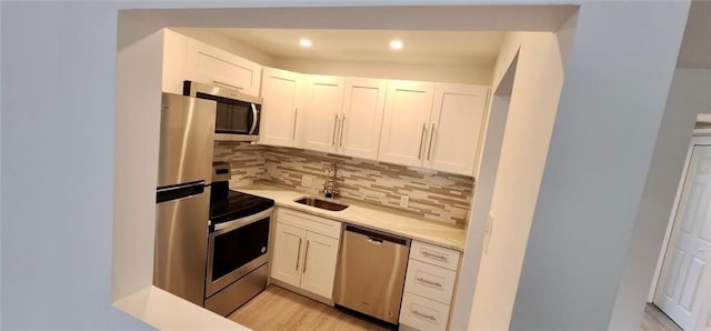 kitchen featuring backsplash, sink, light wood-type flooring, appliances with stainless steel finishes, and white cabinetry