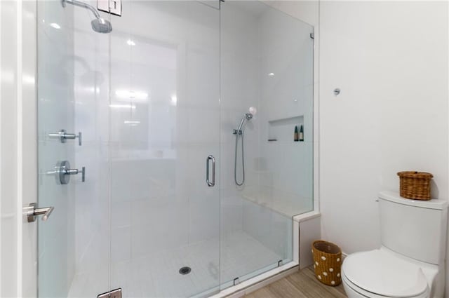 bathroom with hardwood / wood-style floors, a shower with shower door, and toilet