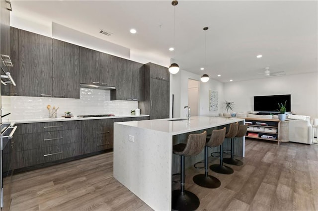 kitchen with pendant lighting, sink, dark wood-type flooring, an island with sink, and a kitchen bar