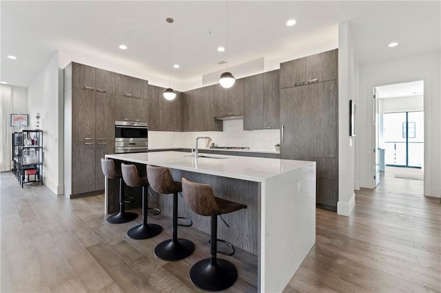 kitchen featuring dark hardwood / wood-style floors, a center island with sink, a kitchen breakfast bar, and decorative light fixtures